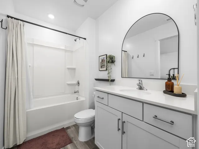 Bathroom featuring a vanity with white cabinetry, a solid surface countertop, an arched mirror, and wood-finish flooring