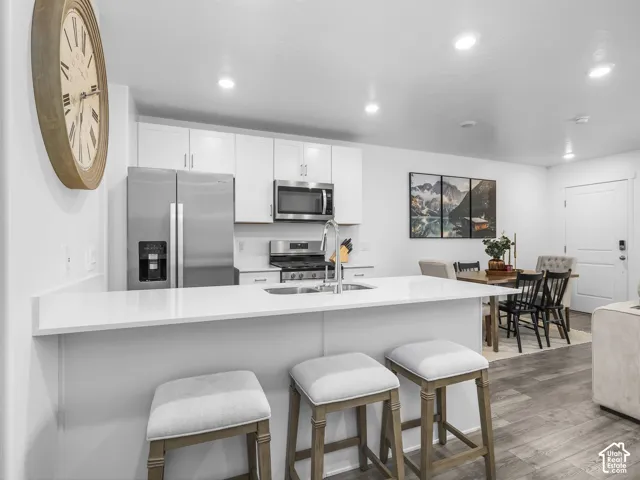 Kitchen featuring white cabinetry, solid-surface countertops, recessed lighting, stainless steel appliances, and wood-finish flooring
