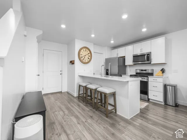 Kitchen featuring white cabinetry, wood-finish flooring, recessed lighting, stainless steel appliances, and a breakfast bar