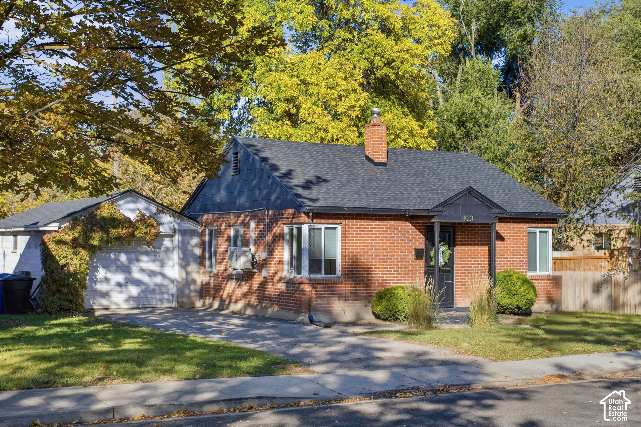 Single-story brick exterior featuring a steep-pitched shingle roof, chimney, bay window, and covered front entryway with an attached garage