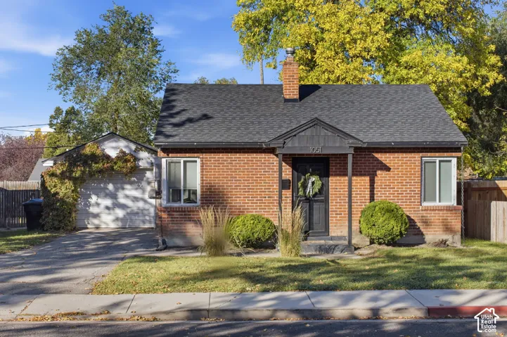 Brick exterior featuring a central chimney, covered front entryway, detached garage, and dual-pane windows