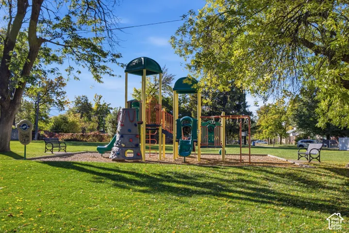 Outdoor recreation area featuring a multi-component play structure, aggregate ground cover, manicured lawn, and mature trees