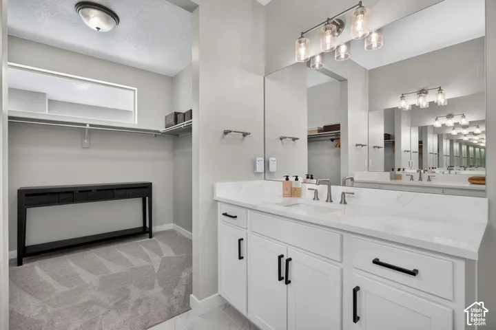 White cabinetry with black hardware, stone-finish vanity top with undermount sink, multi-light vanity fixture, wall-to-wall mirror, and wall-mounted closet shelving
