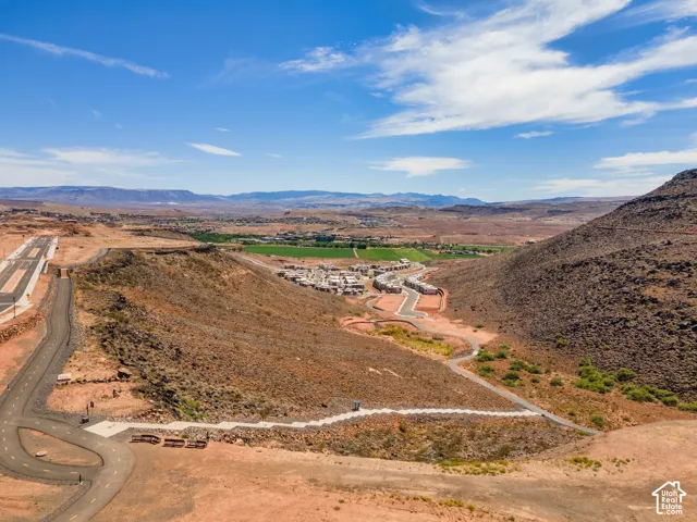 Aerial perspective of high-desert terrain featuring paved asphalt roadways, concrete pedestrian pathways, expansive natural rock formations, and mountain backdrops