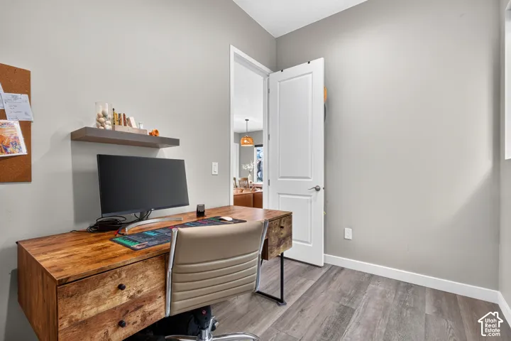 Neutral interior space featuring wood-finish flooring, a wall-mounted floating shelf, and a white two-panel interior door with brushed metal hardware