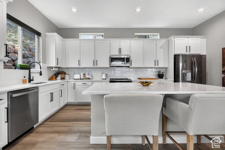 Kitchen featuring white cabinetry, an expansive central island with stone-finish countertops, wood-finish flooring, stainless steel appliances, and a matte black faucet