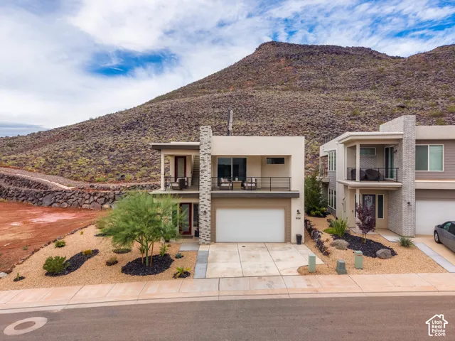 Contemporary exterior featuring a stone-clad chimney, upper-level covered balcony with metal railing, and concrete driveway