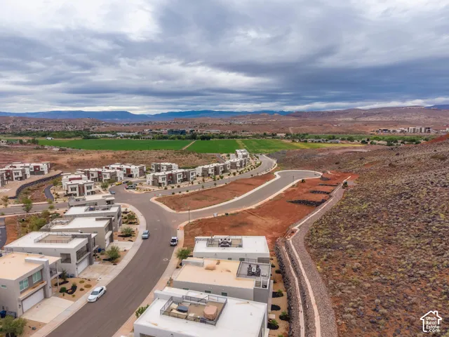 Aerial perspective of a multi-unit residential development featuring contemporary flat-roof architecture, paved streets, drought-tolerant desert landscaping, and prominent mountain backdrops
