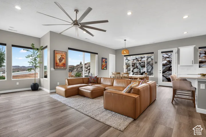 Open-concept interior featuring wood-finish flooring, recessed lighting, a large-format ceiling fan, expansive windows with natural scenery, and a kitchen peninsula with bar seating