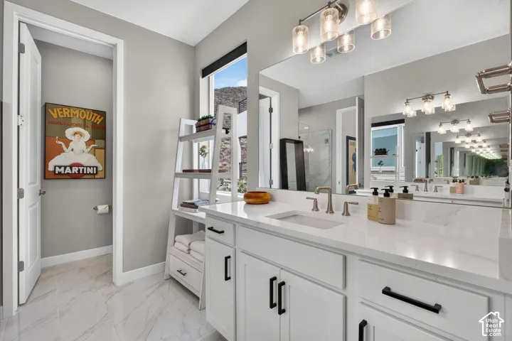 White cabinetry with matte black hardware, stone-finish countertop, undermount sink, multi-light vanity fixture, and large wall-mounted mirror