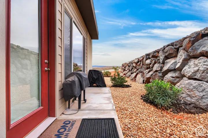 Concrete patio with a red-framed glass exterior door, horizontal siding, and a stacked stone retaining wall set against a landscaped gravel ground cover