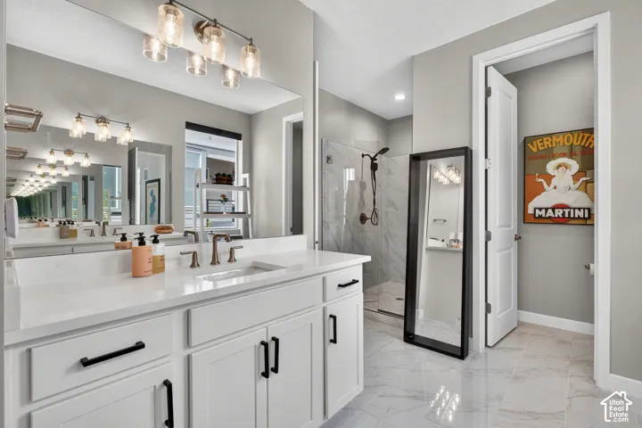 White shaker-style cabinetry with matte black hardware, stone-composite countertop, dual-faucet vanity, full-width mirror, and walk-in shower with tile surround