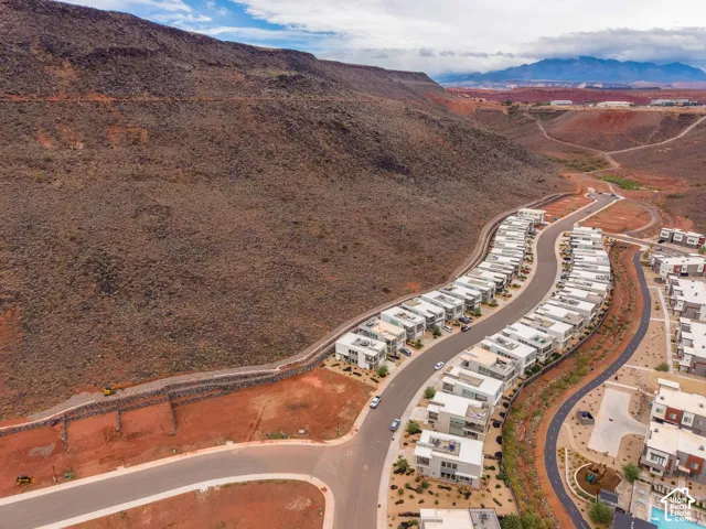 Aerial perspective of a multi-unit residential development featuring modern flat-roof architecture, paved thoroughfares, and a prominent mountain range backdrop