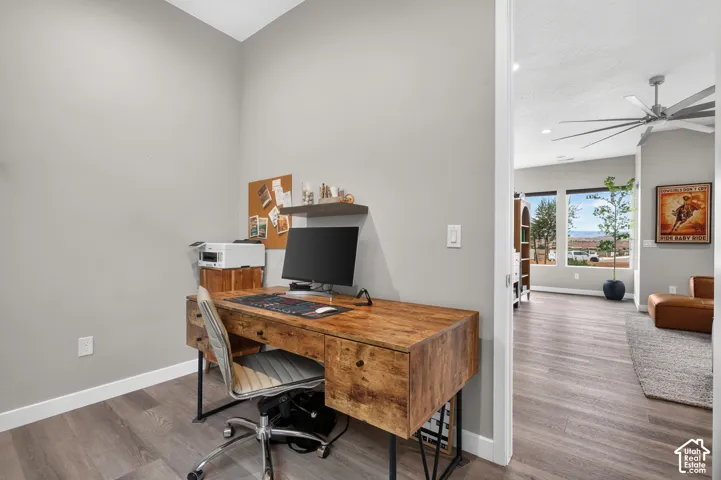 Neutral-toned interior featuring wood-finish flooring, a wall-mounted floating shelf, and a ceiling fan with integrated lighting
