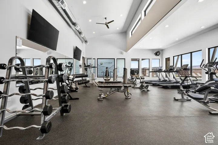 Fitness space featuring high vaulted ceilings, expansive floor-to-ceiling windows, exposed industrial ductwork, recessed lighting, and durable rubberized flooring