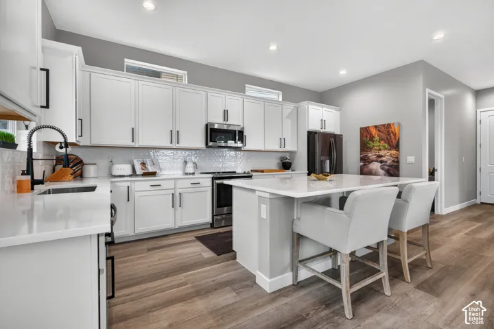 Kitchen featuring white cabinetry with matte black hardware, quartz countertops, white subway tile backsplash, stainless steel appliances, and wood-finish flooring