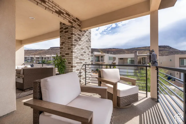 Covered balcony featuring exposed brick columns, recessed lighting, horizontal metal railings, and a backdrop of mountain scenery