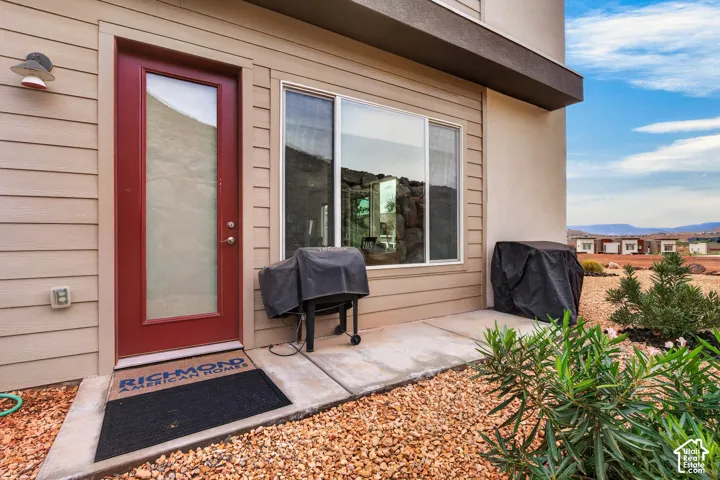 Exterior patio featuring horizontal lap siding, a red glass-panel door, large window with multi-pane configuration, and desert-style gravel landscaping