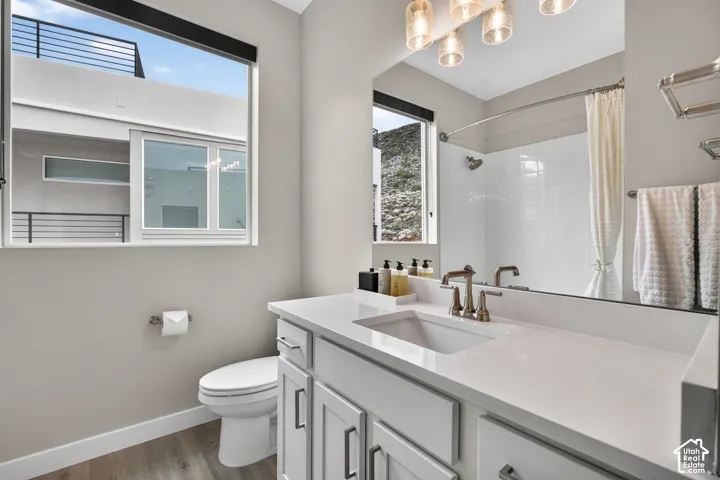 Vanity with a solid-surface countertop and undermount sink, shaker-style cabinetry with metallic hardware, wood-finish flooring, and a large-format mirror with multi-bulb light fixture