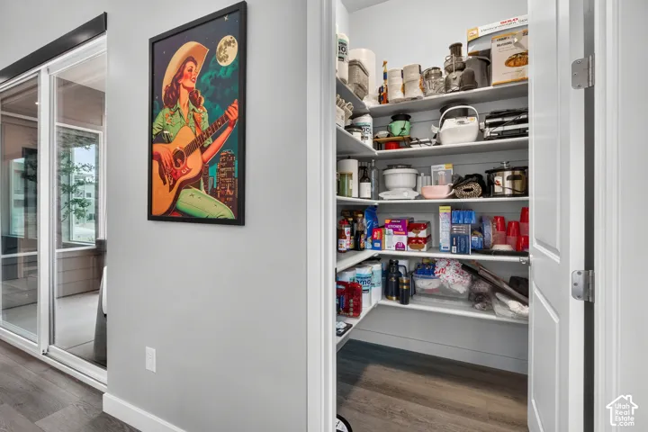 Walk-in pantry featuring white shelving with shiplap-style back paneling and wood-finish flooring