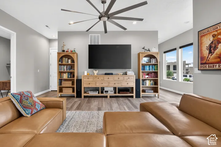 Living area featuring wood-finish flooring, a multi-blade ceiling fan, and large windows