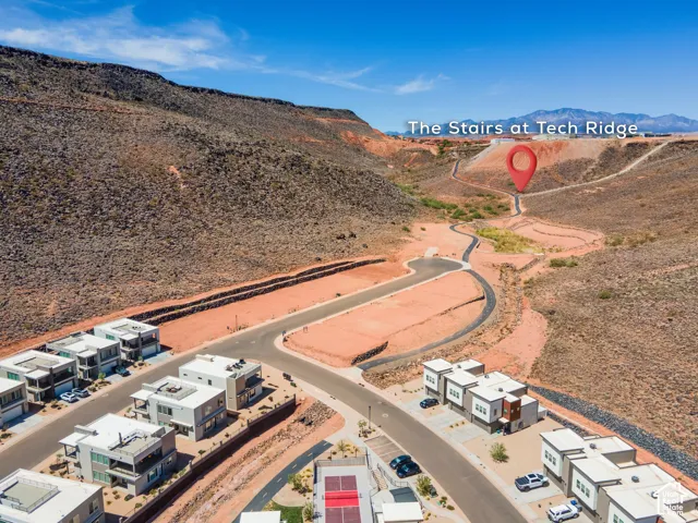 Aerial perspective of multi-level residential structures featuring flat rooflines, paved access roads, and a paved pedestrian pathway extending toward mountainous terrain