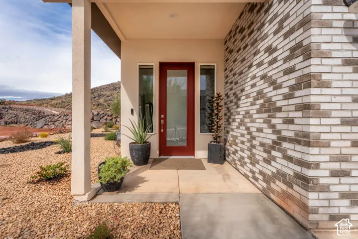 Covered entryway featuring a red-framed glass door, flanking sidelights, and multi-tone brick siding