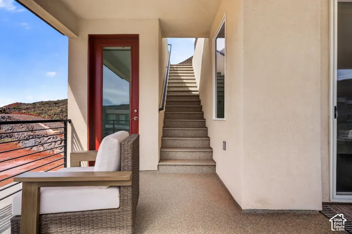 Covered terrace featuring a textured finish, red-trimmed glass entry door, metal railing, and an external staircase