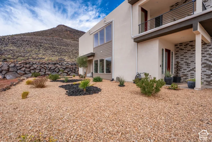 Modern two-story exterior featuring a stucco facade, brick veneer accents, metal balcony railing, and large windows set against a mountain landscape