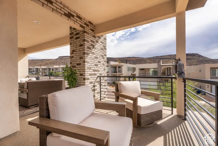 Covered outdoor balcony featuring brick support columns, recessed ceiling lighting, a metal horizontal rail system, and mountain terrain backdrop