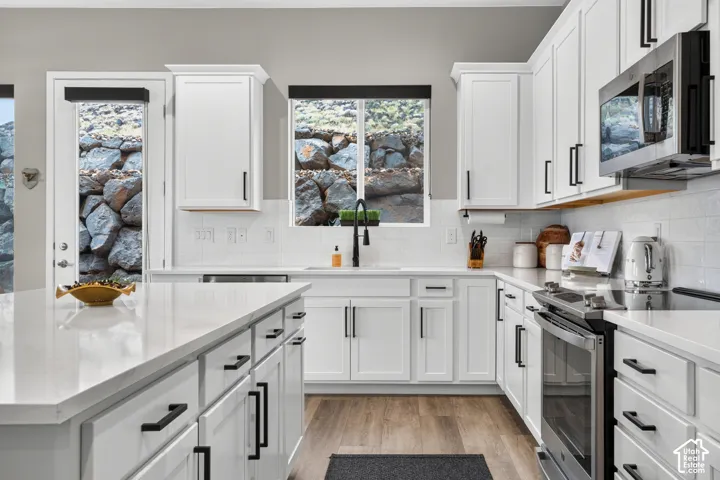 Kitchen featuring white shaker-style cabinetry, white countertops, a central island, stainless steel appliances, and a tile backsplash