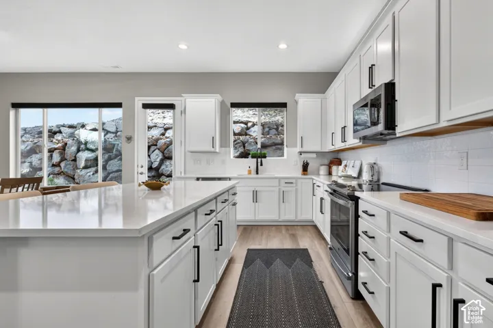Kitchen featuring white Shaker-style cabinetry, a quartz-topped center island, light-toned wood-finish flooring, matte black hardware, and stainless steel appliances