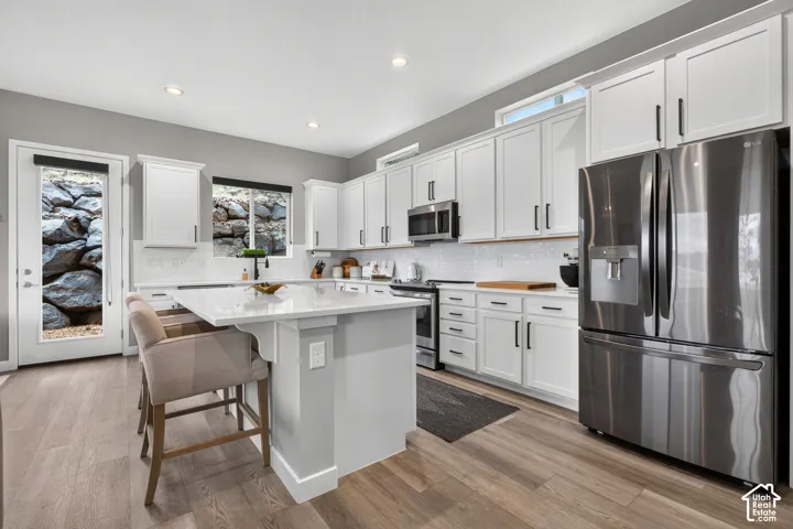 Kitchen featuring white shaker cabinetry, quartz countertops, a central island with an integrated breakfast bar, stainless steel appliances, and wood-finish flooring