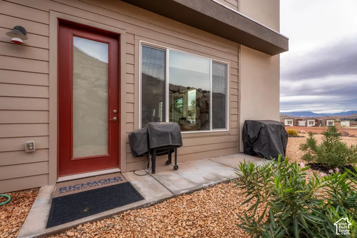 Exterior featuring horizontal siding, a red-finished glass-paneled door, a large window, a concrete patio, and xeriscaped grounds with mountain scenery