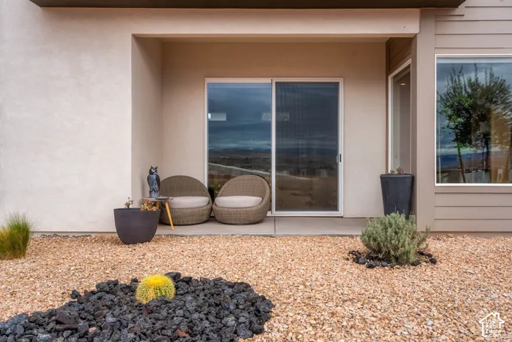 Covered patio featuring a concrete slab foundation, sliding glass door, smooth stucco exterior, and xeriscaped ground cover with decorative stone accents