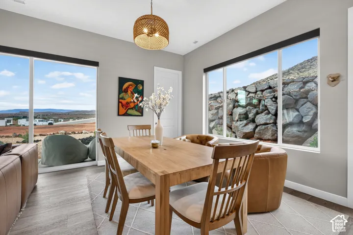 Dining area featuring expansive floor-to-ceiling windows, wood-finish flooring, a woven drum pendant light fixture, and a natural stone retaining wall backdrop