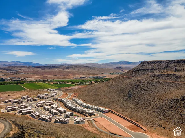 Aerial perspective of a multi-unit residential community surrounded by expansive desert terrain, rock formations, and mountain ranges