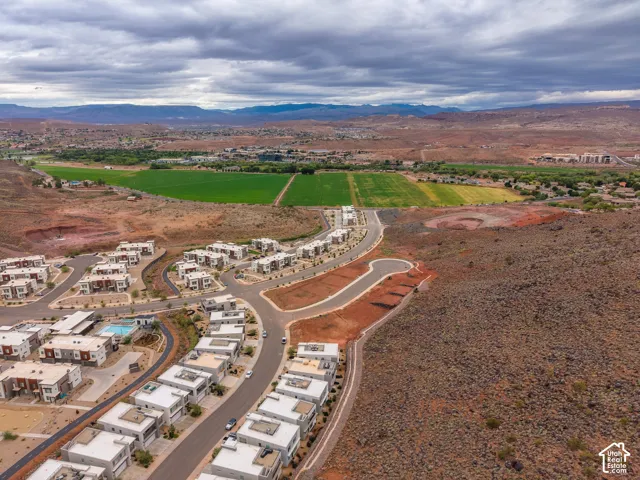 Aerial perspective of a multi-residence community featuring modern flat-roof architecture, paved street infrastructure, and desert landscape surroundings with mountain backdrops