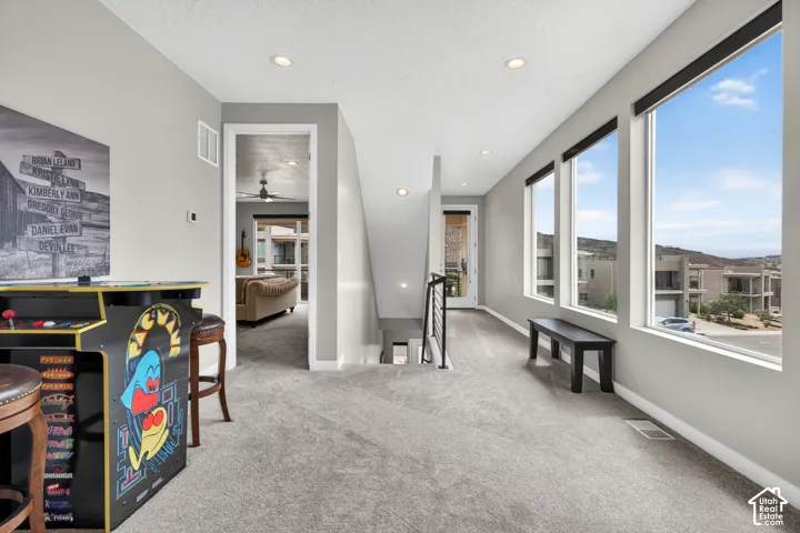 Open loft featuring neutral carpeting, recessed ceiling lighting, and large windows with prominent hill scenery