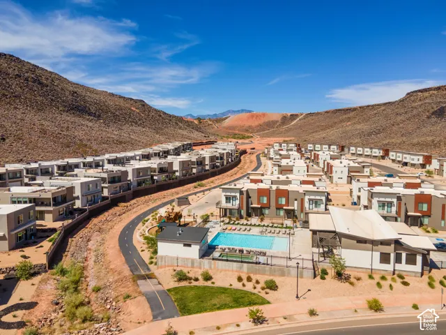 Aerial perspective of a multi-unit development featuring a communal swimming pool, paved walking path, desert landscaping, and mountain backdrop