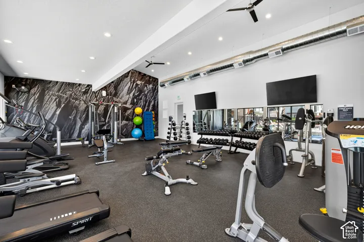 Fitness room featuring rubberized flooring, industrial-style exposed metal ductwork, recessed lighting, ceiling-mounted fans, and wall-mounted televisions