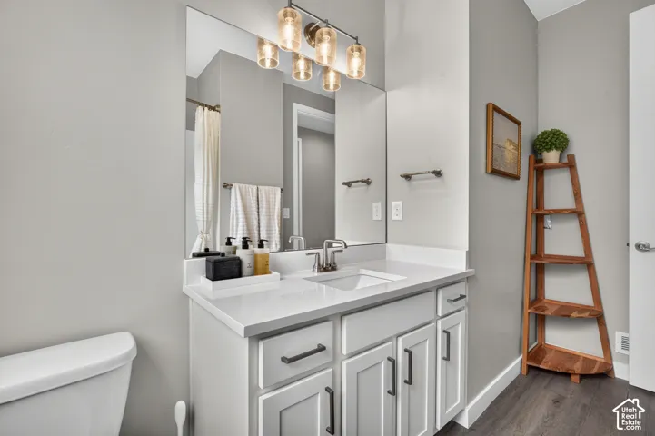 Bathroom featuring a vanity with white cabinetry, a light-toned countertop, an integrated rectangular sink, dark hardware, and a multi-light fixture over a large mirror