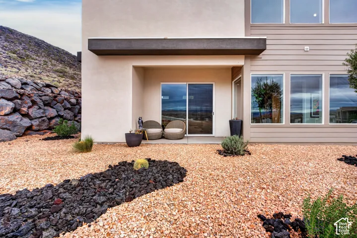 Stucco and horizontal siding exterior featuring a concrete patio, sliding glass door, oversized windows, and landscaped rock terrain