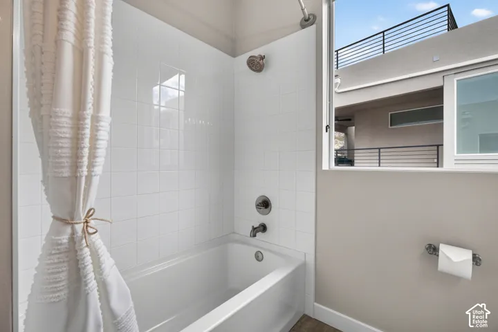 Bathroom featuring a white tile tub surround, metallic finish plumbing fixtures, a recessed shower head, and a large window