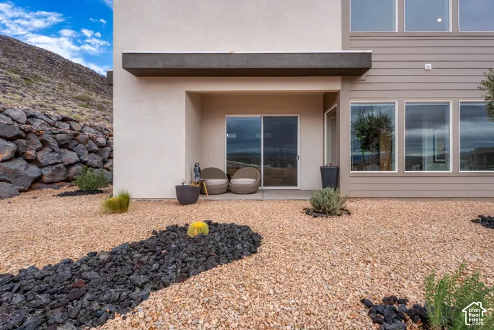 Exterior featuring stucco and horizontal siding, a covered concrete patio, sliding glass door, and xeriscaped grounds with a stone retaining wall