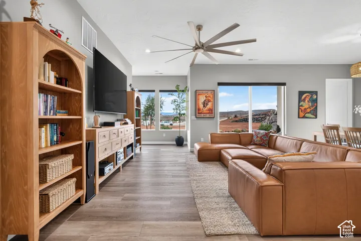 Open-concept living space featuring wood-finish flooring, a multi-blade ceiling fan, recessed lighting, and large windows with outdoor landscape scenery