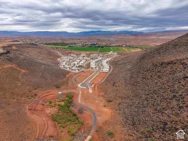 Aerial perspective of a multi-unit residential development nestled within a desert basin, characterized by paved roadways and proximity to expansive mountain landscapes and greenbelt terrain
