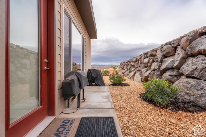 Concrete patio featuring horizontal siding, red-framed glass exterior door, and a natural stone retaining wall set against a gravel landscape