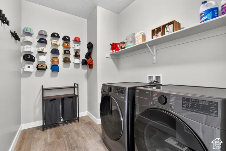 Laundry room featuring wood-finish flooring, a wall-mounted floating shelf, and multiple black wall hooks