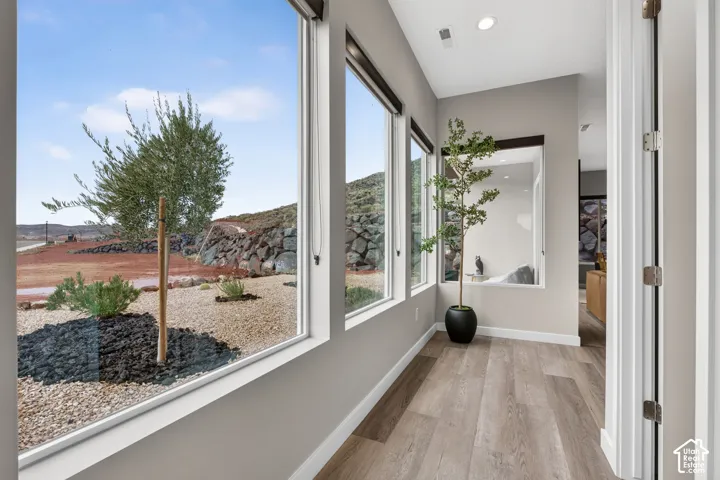 Expansive windows providing natural light and exterior landscape imagery, complemented by wood-finish flooring and recessed ceiling lighting